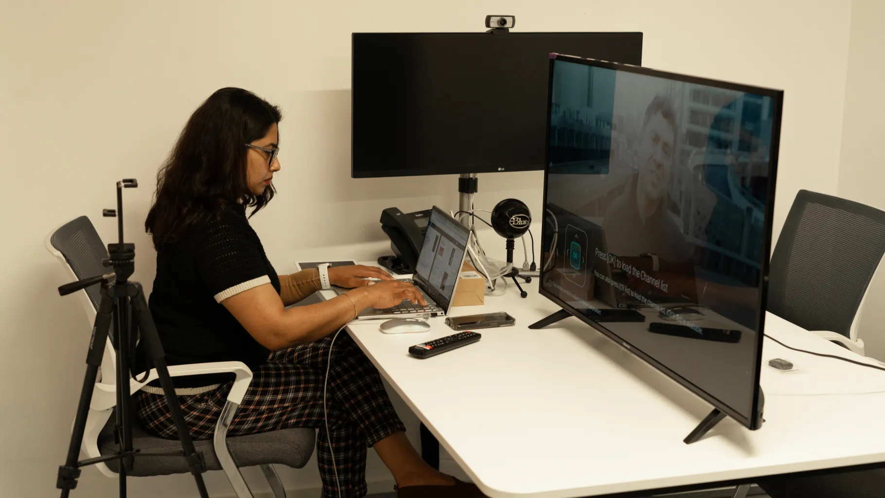 A tester at a desk with a laptop and a TV, set up with a camera and microphone in the testing room