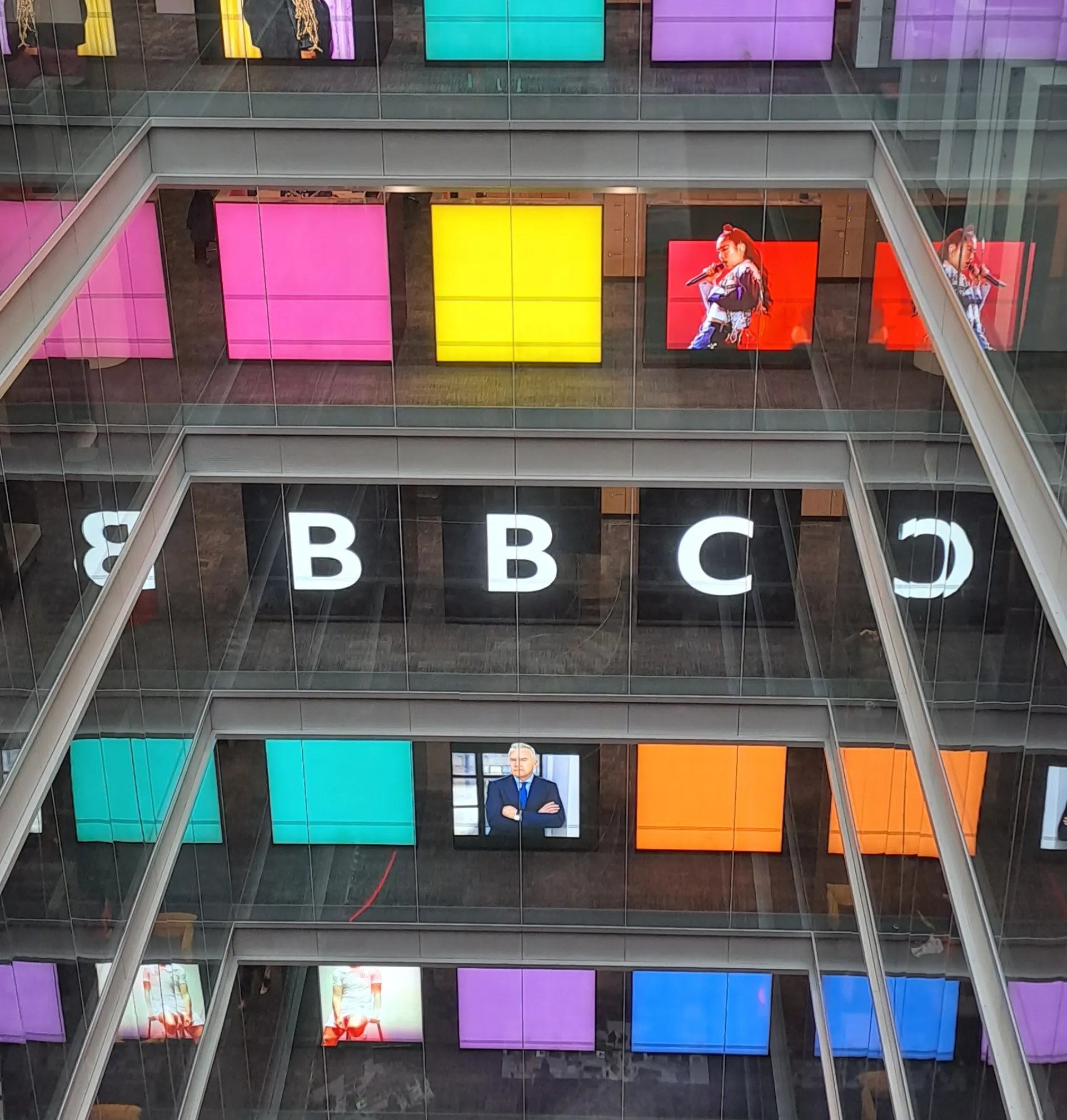 The atrium of BBC Broadcasting House, its floors lined with coloured screens and the BBC letters