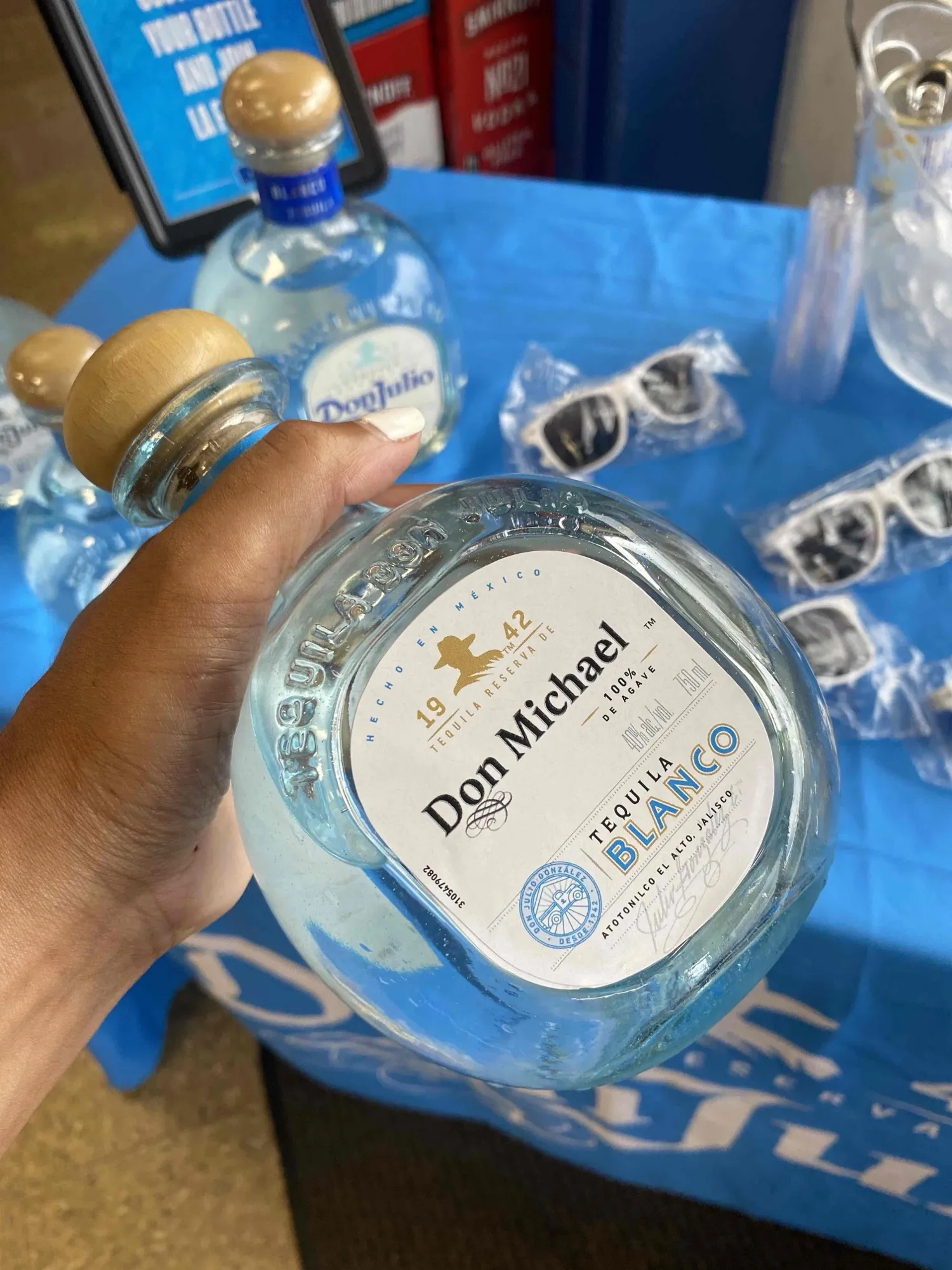 A hand holding a Don Julio Blanco bottle with a personalised Don Michael label, at a promotional stand